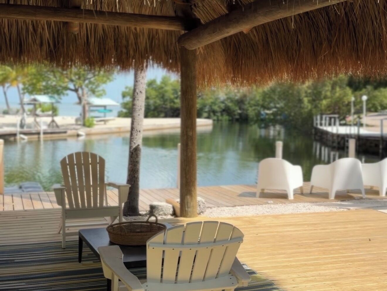A wooden deck with a thatched roof, white chairs, and a view of a body of water.