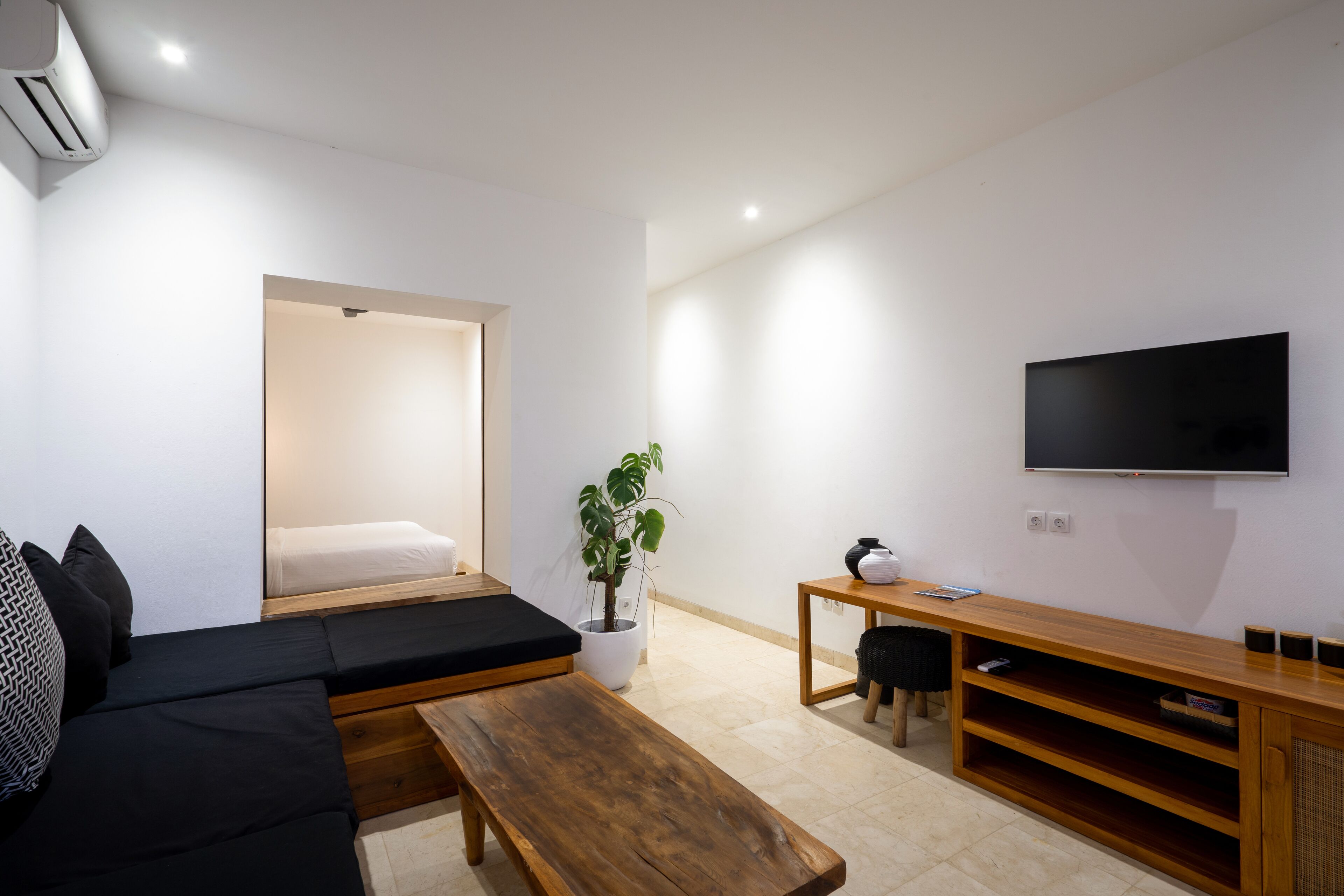 Una sala de estar moderna con un sofá, una mesa de centro de madera, un televisor y una planta en maceta.