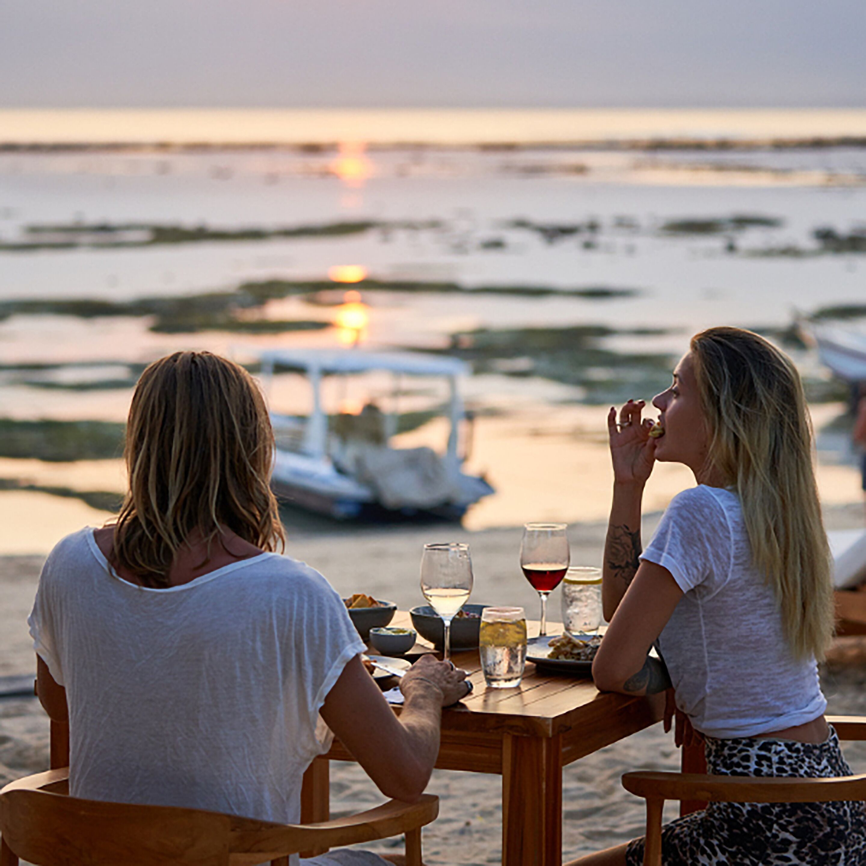 Two people dining at a wooden table with a view of the sea and boats in the background.