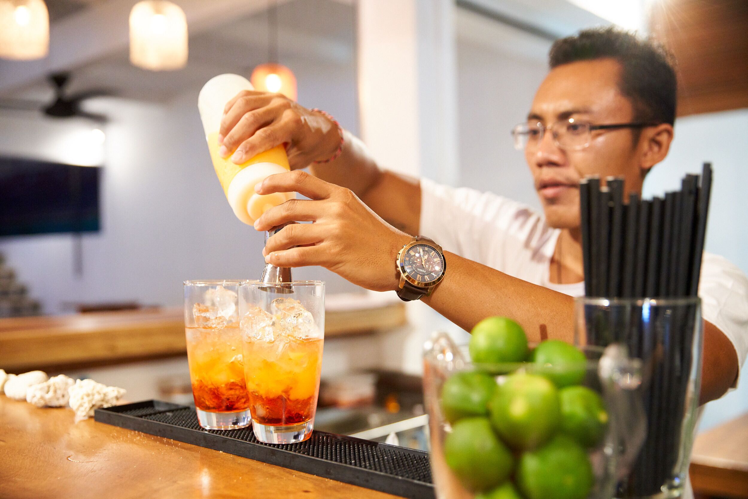 Een bartender bereidt een drankje toe met een cocktailshaker en twee glazen op een bargedeelte.