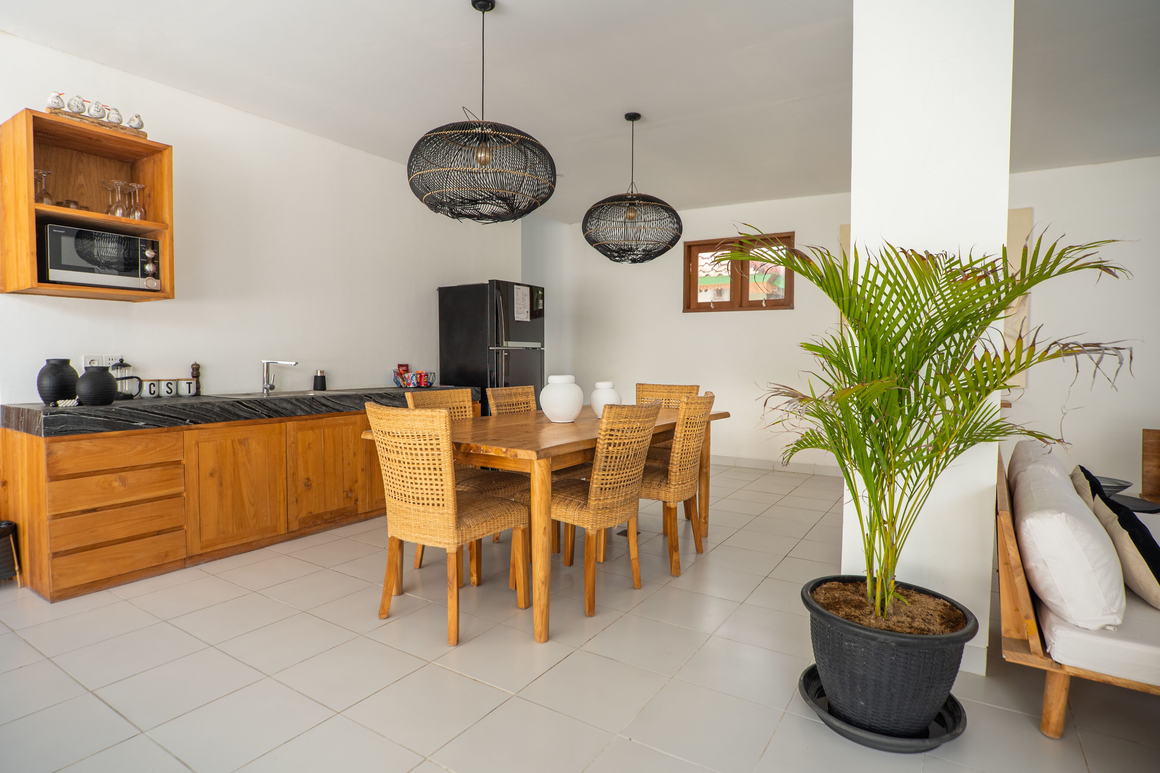 Een moderne keuken met houten kasten, een eettafel met rieten stoelen en een potplant.