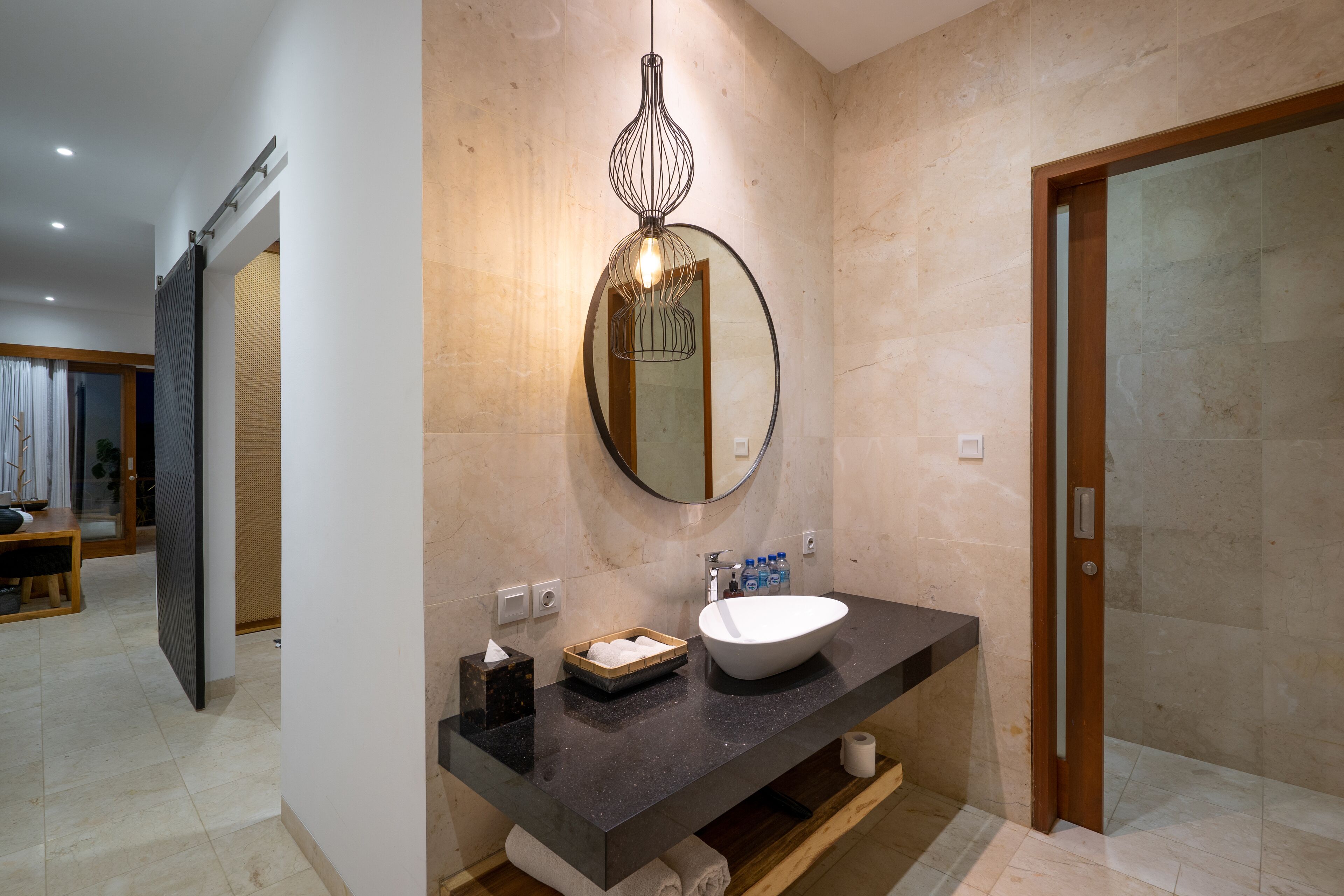 Een moderne badkamer met een grote spiegel, een ronde hanglamp, een wit wastafelmeubel en een houten deur.