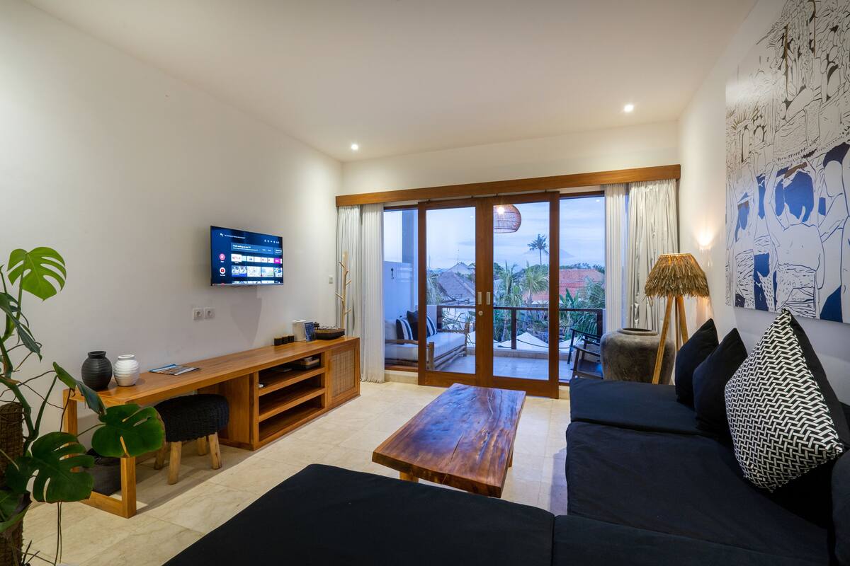 A modern living room with a wooden coffee table, black sofa, and a TV mounted on the wall.