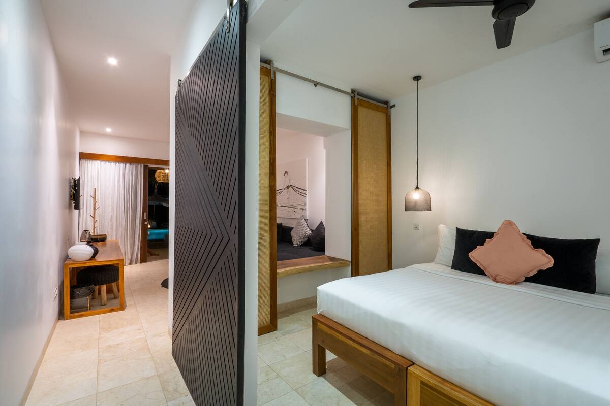 A modern bedroom with a bed, bedside table, and a view of a bathroom.
