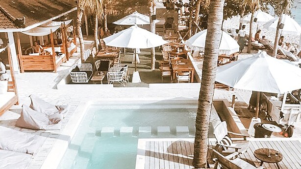 A pool area with lounge chairs and umbrellas, surrounded by palm trees and a wooden deck.