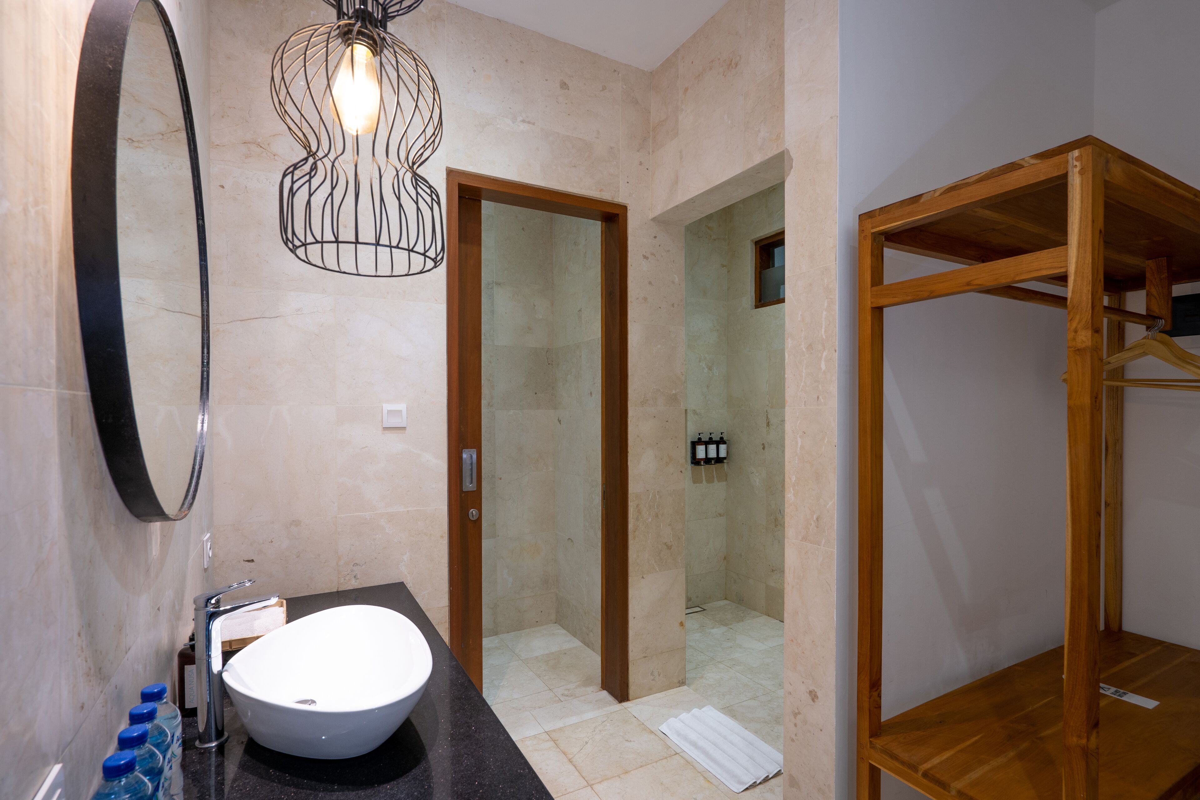 A bathroom with a large sink, mirror, shower, and wooden shelving unit.