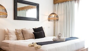 A bedroom with a wooden bed frame, white bedding, a mirror above the bed, and two hanging lamps.