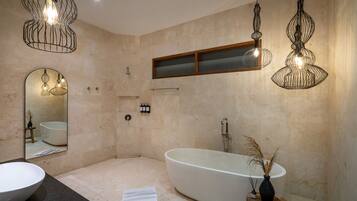 A modern bathroom with a freestanding bathtub, a large mirror, and pendant lighting fixtures.