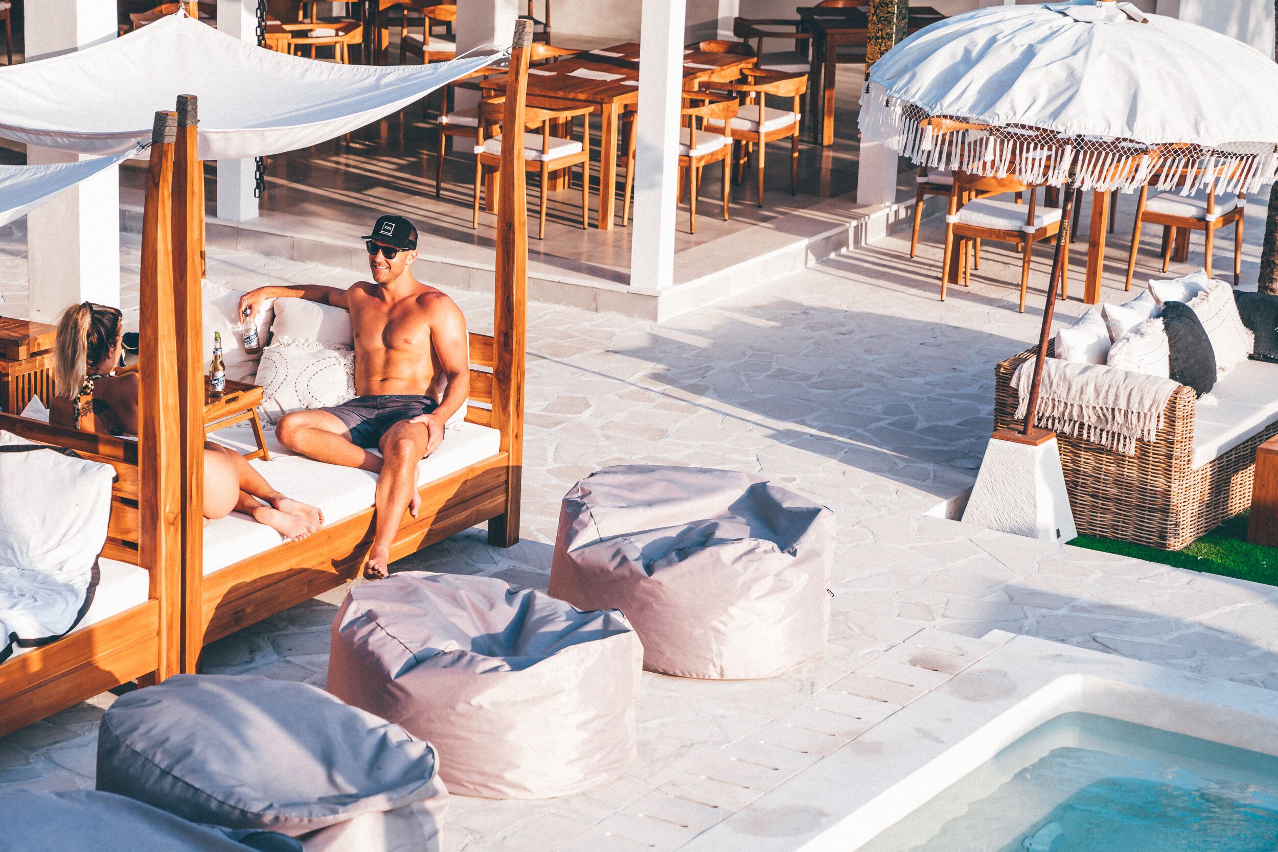 A poolside area with wooden loungers, covered seating, and a hot tub.