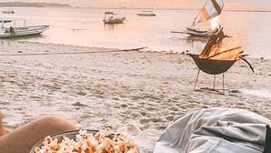 A beach scene with a campfire, boats, and a bowl of popcorn.