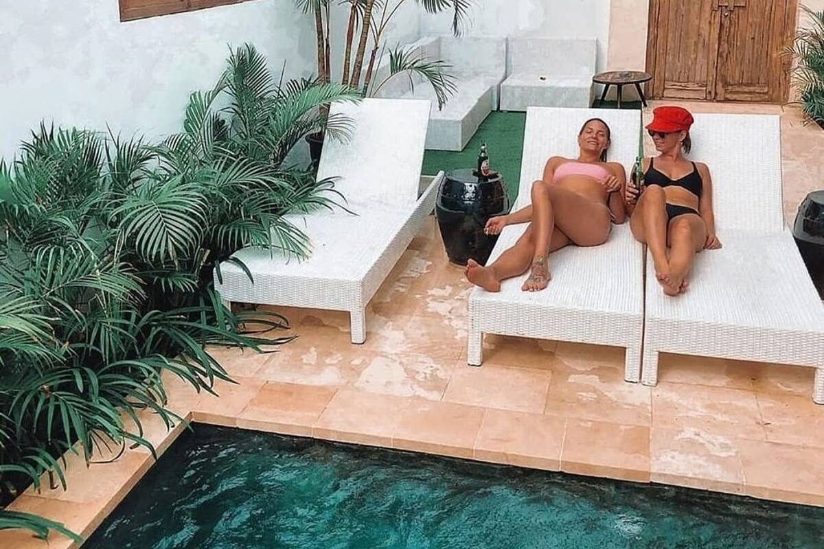 Two lounge chairs with a pool in the foreground and potted plants around.