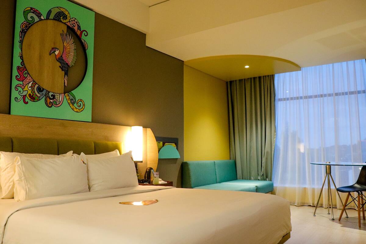 A hotel room with a large bed, a green sofa, a small table, and a chair.