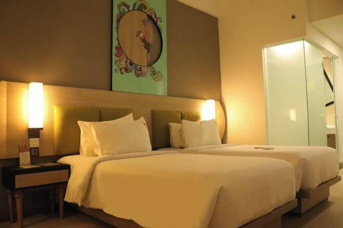 A hotel room with two beds, a nightstand, a wall clock, and a door.