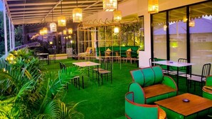 An indoor seating area with tables and chairs, a green artificial grass floor, and hanging light fixtures. - MaxOneHotels.com at Balikpapan (Balikpapan)
