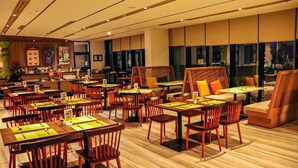 A modern restaurant with wooden tables and chairs, a bar area, and large windows offering city views. - MaxOneHotels.com at Balikpapan (Balikpapan)