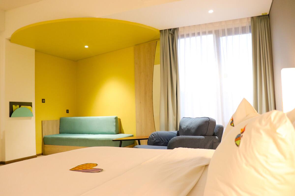 A hotel room with a bed, a sofa, a desk, and a window with curtains.