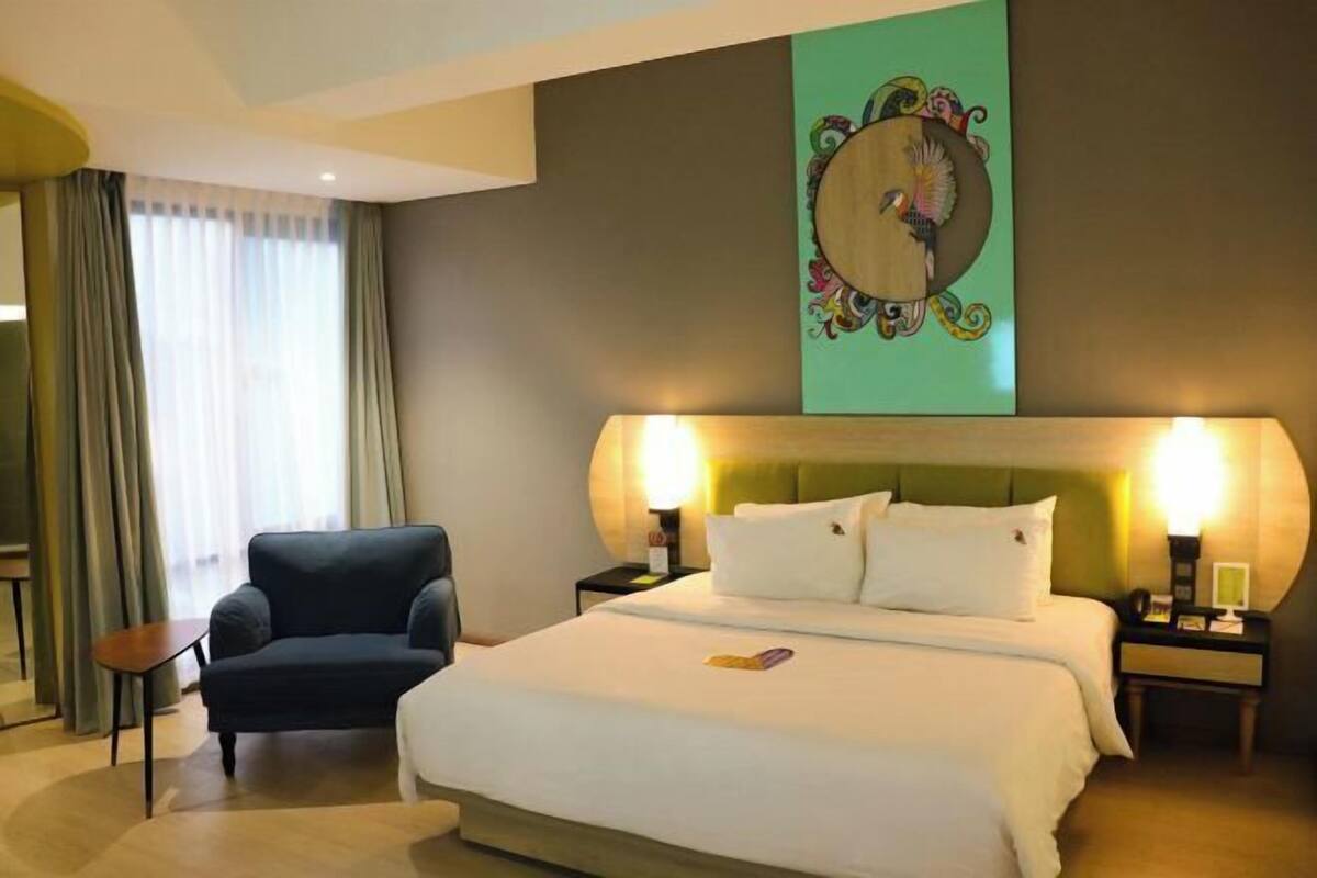 A hotel room with a bed, a chair, a nightstand, and a wall-mounted artwork.