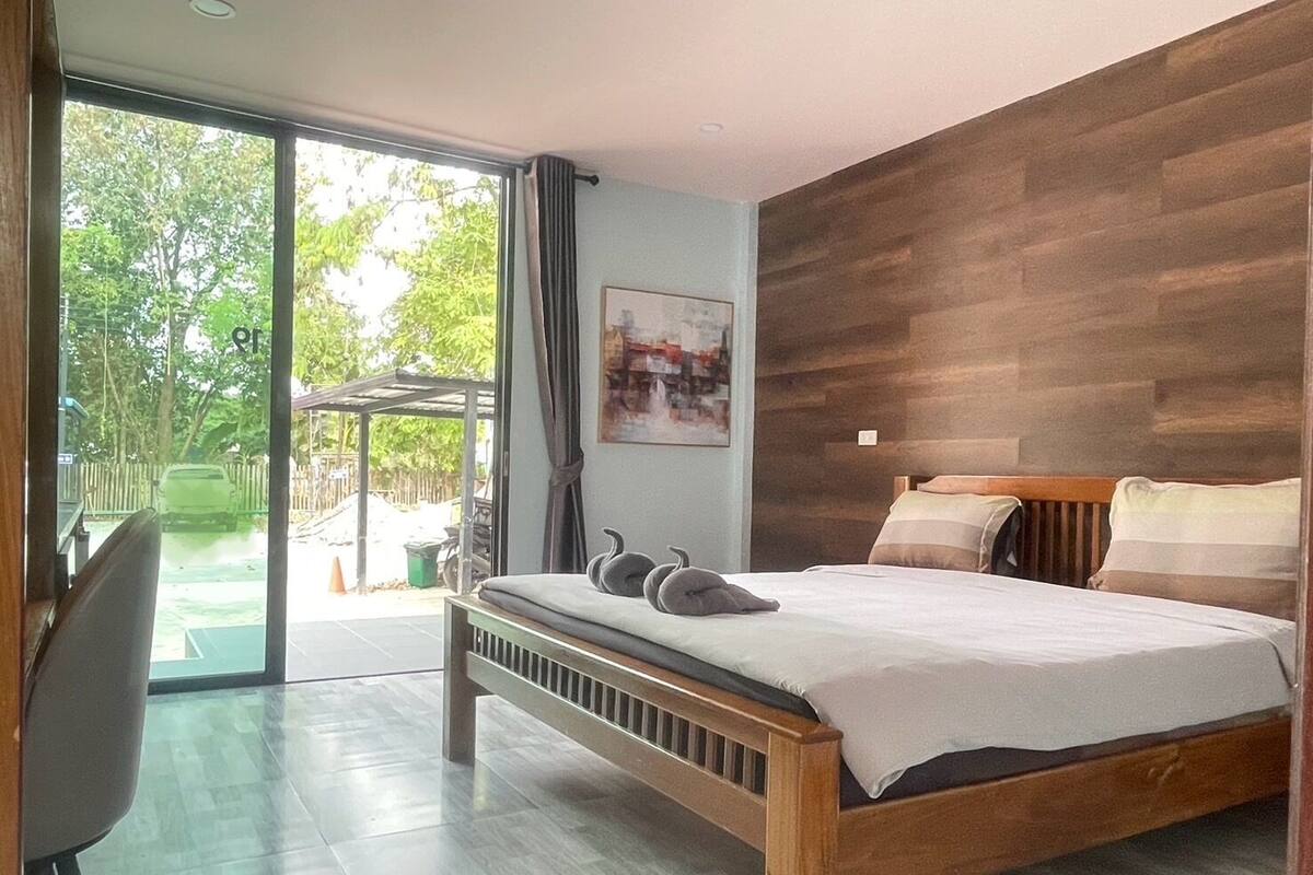 A modern bedroom with a wooden bed, a large window, and a view of the outdoors.