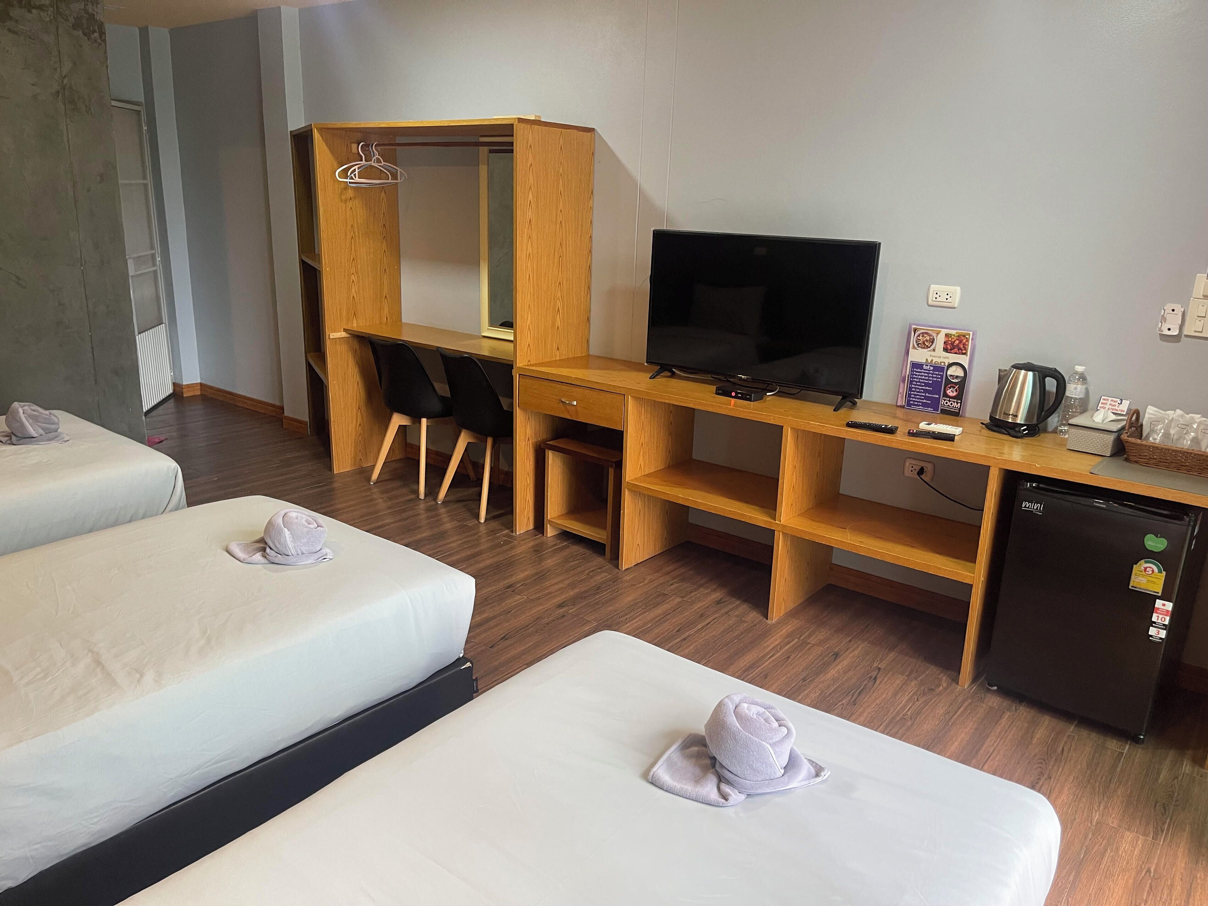 Een hotelkamer met twee bedden, een houten bureau met een televisie, een kleine koelkast en een waterkoker.