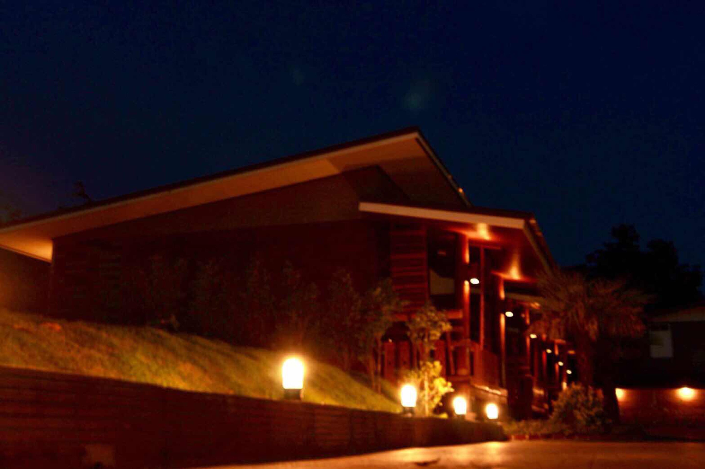 A modern house with a sloped roof, a brick exterior, and multiple illuminated windows at night.