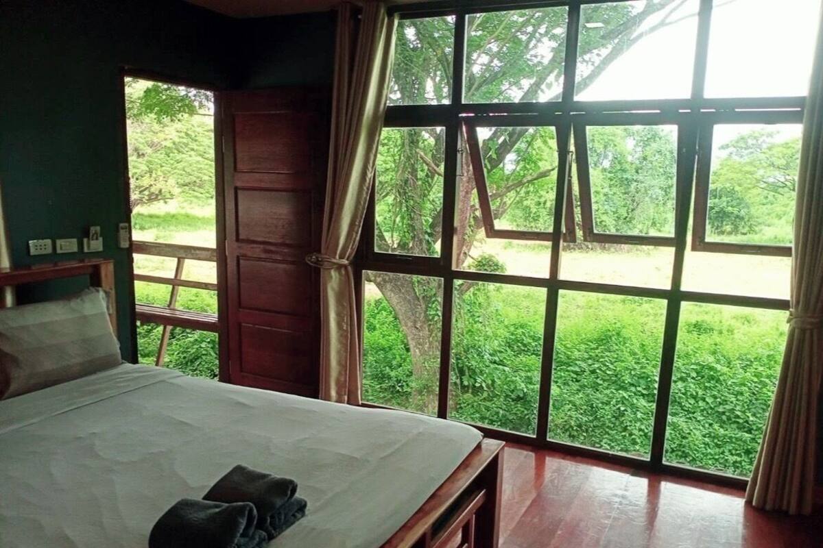 A bedroom with a large window, wooden bed, and curtains.