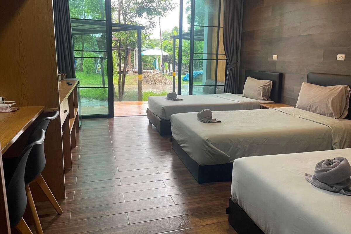 A hotel room with two beds, a desk, and a large sliding glass door leading to an outdoor area.