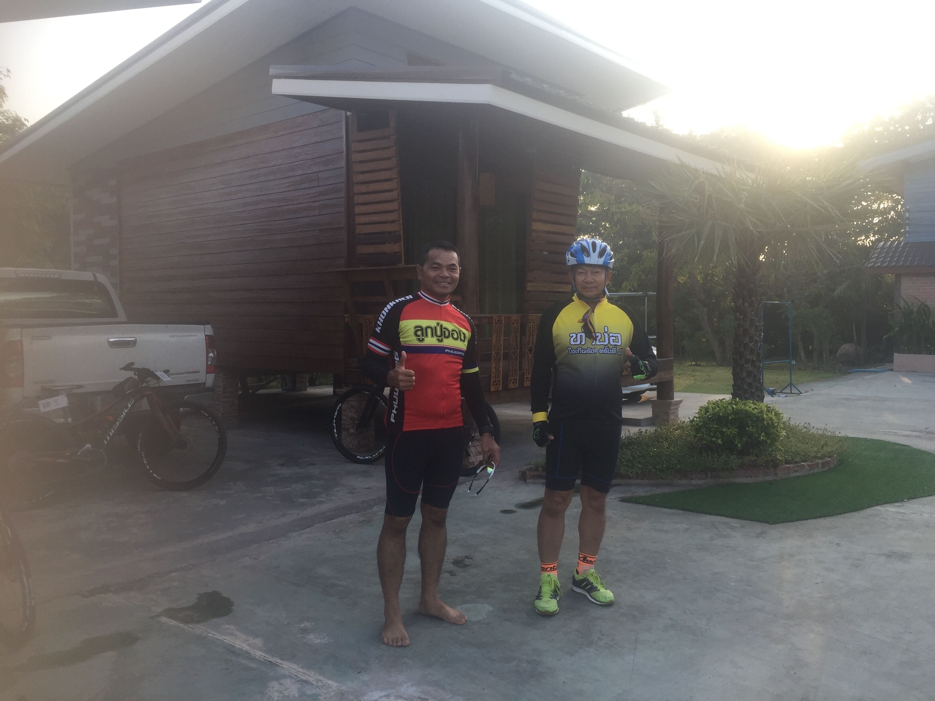 Two people standing in front of a wooden house with a truck parked nearby.