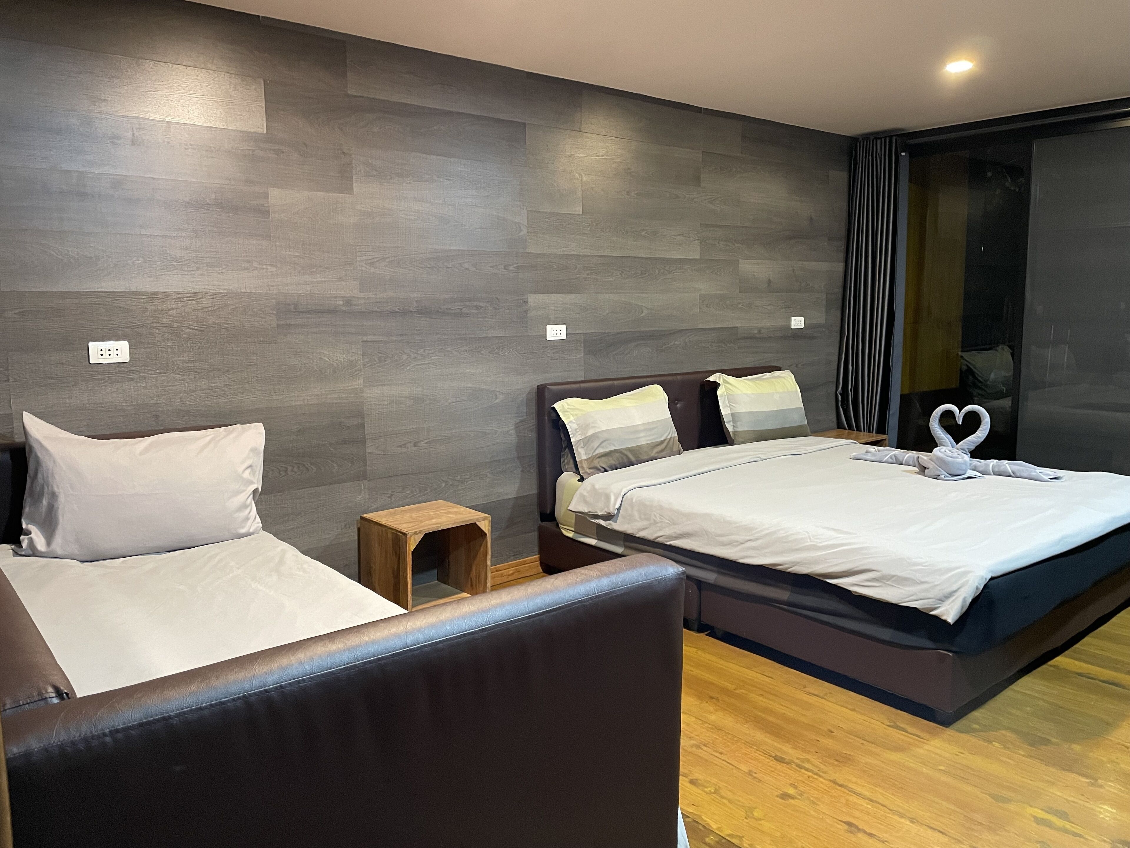 A modern hotel room with two beds, a small wooden nightstand, and a large window with curtains.