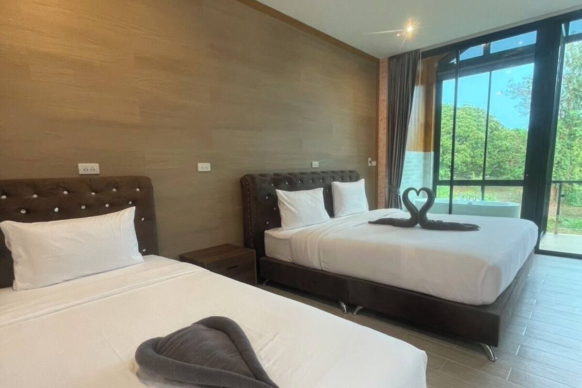 A hotel room with two beds, a large window, and a view of greenery outside.