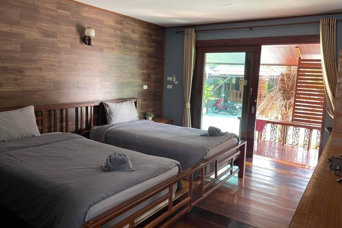 A hotel room with two beds, wooden flooring, a balcony with a view, and a sliding door to the outside.