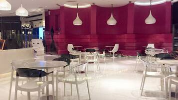 A modern interior with white tables and chairs, a pink wall, and pendant lighting.