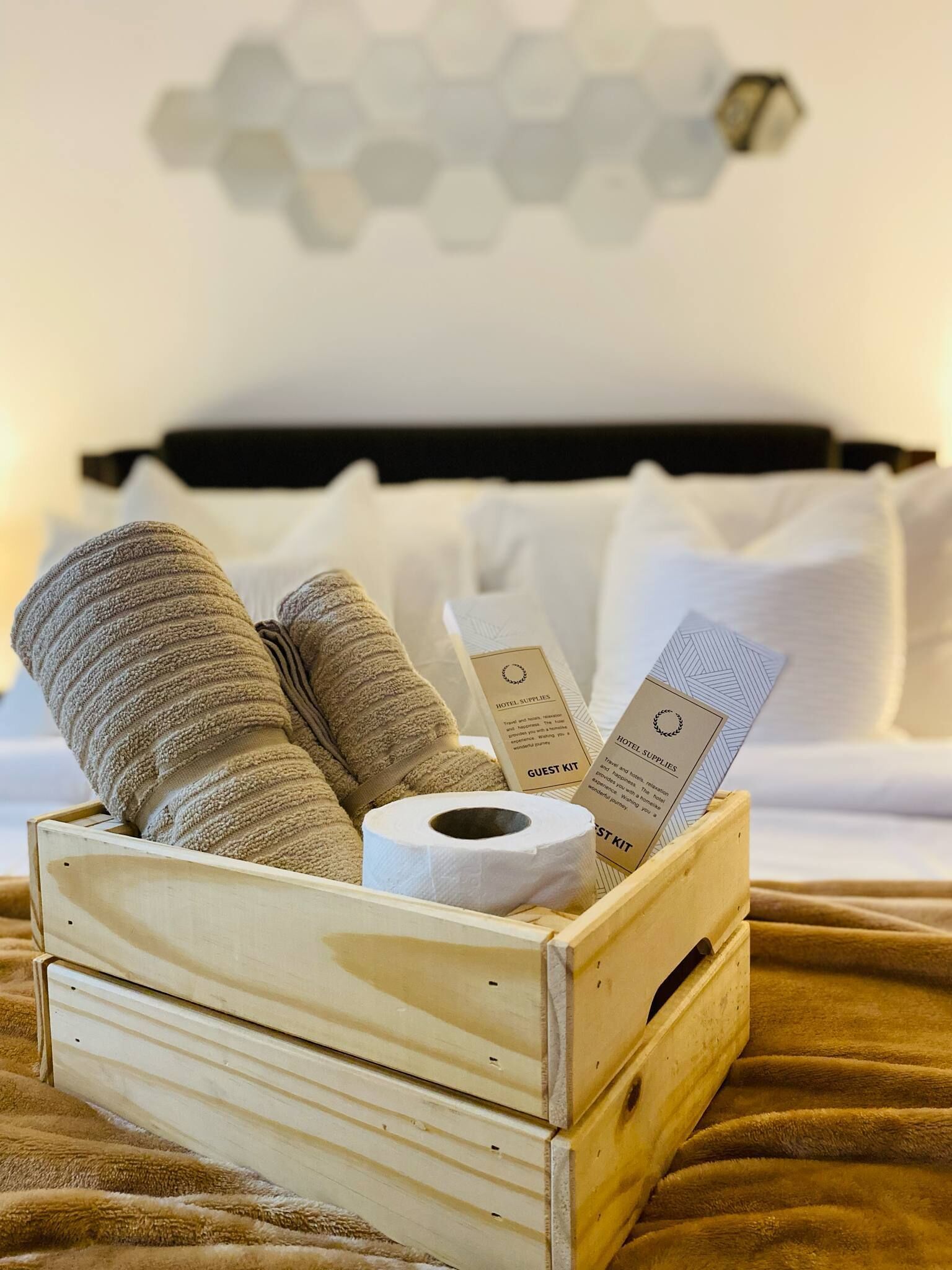 A wooden crate with towels, a roll of toilet paper, and hotel supply cards on a bed.