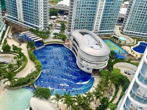 A large swimming pool surrounded by palm trees and modern buildings. - Azure Beach Club Paris Hilton (Parañaque)