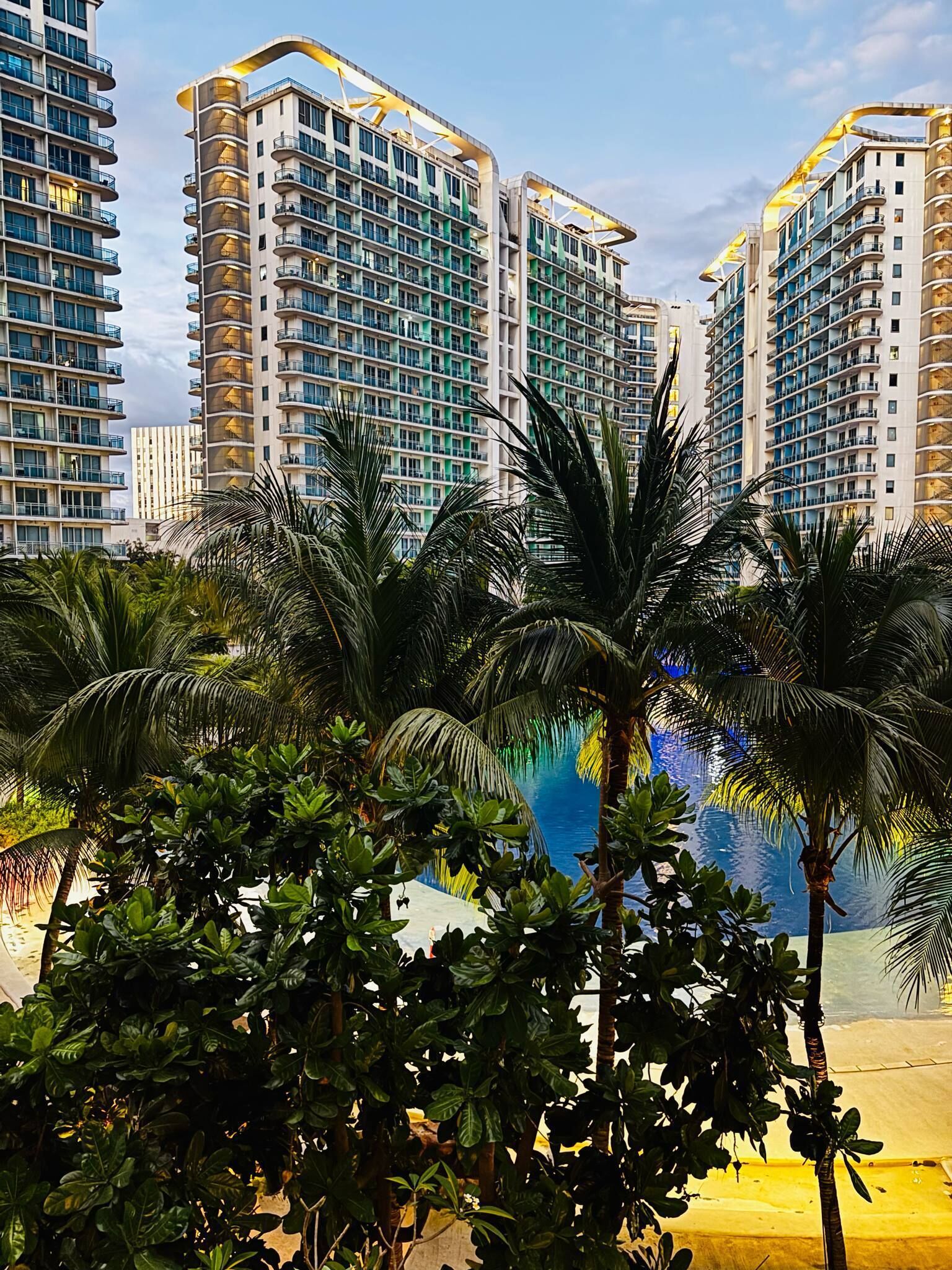 Un moderno edificio de gran altura con múltiples balcones y un área de piscina rodeada de exuberante vegetación.
