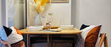 A dining area with a wooden table, two chairs, a vase with dried flowers, and a mirror on the wall.