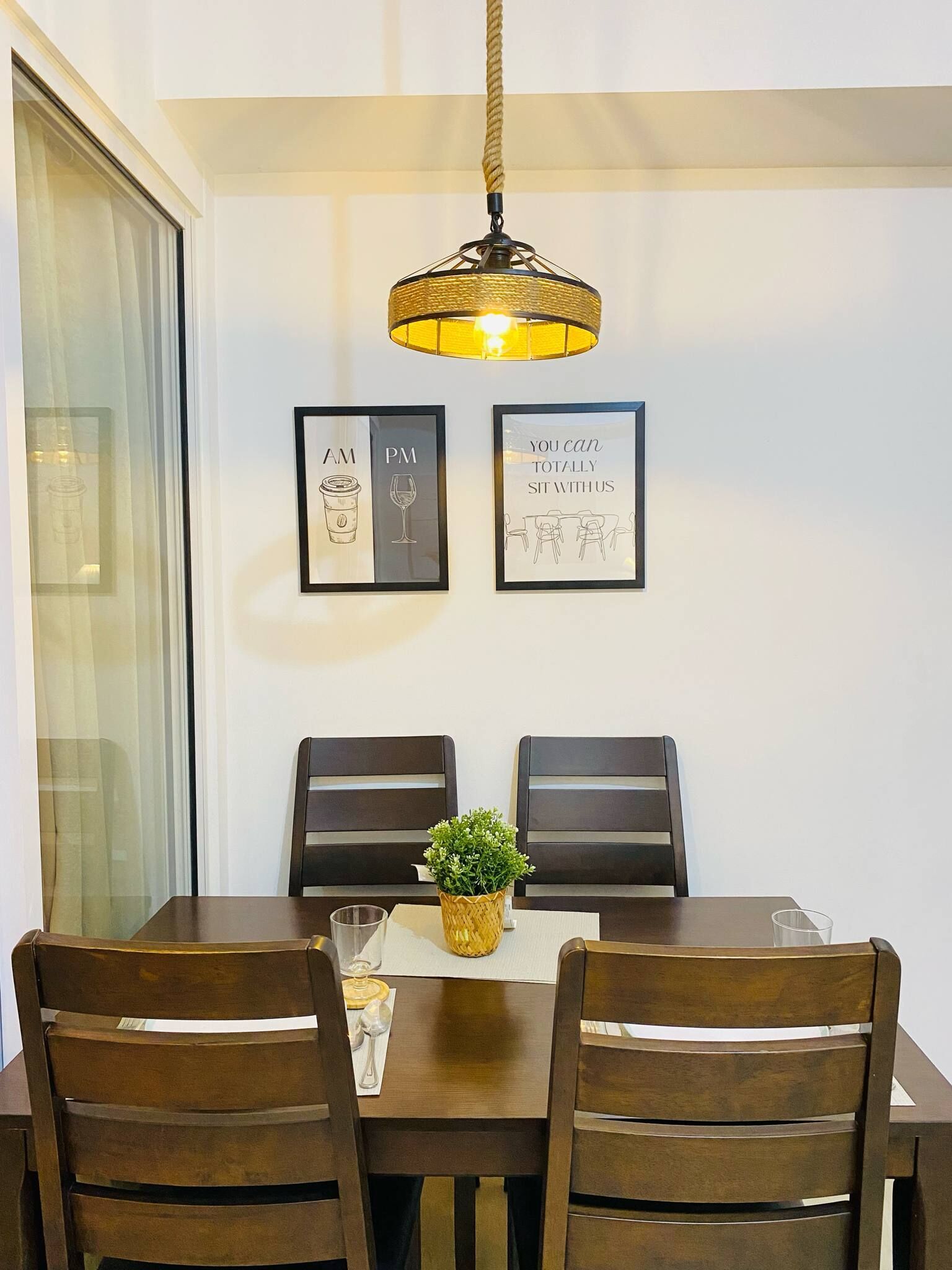 Un coin repas comprenant une table, des chaises, un luminaire suspendu et deux tableaux encadrés accrochés au mur.