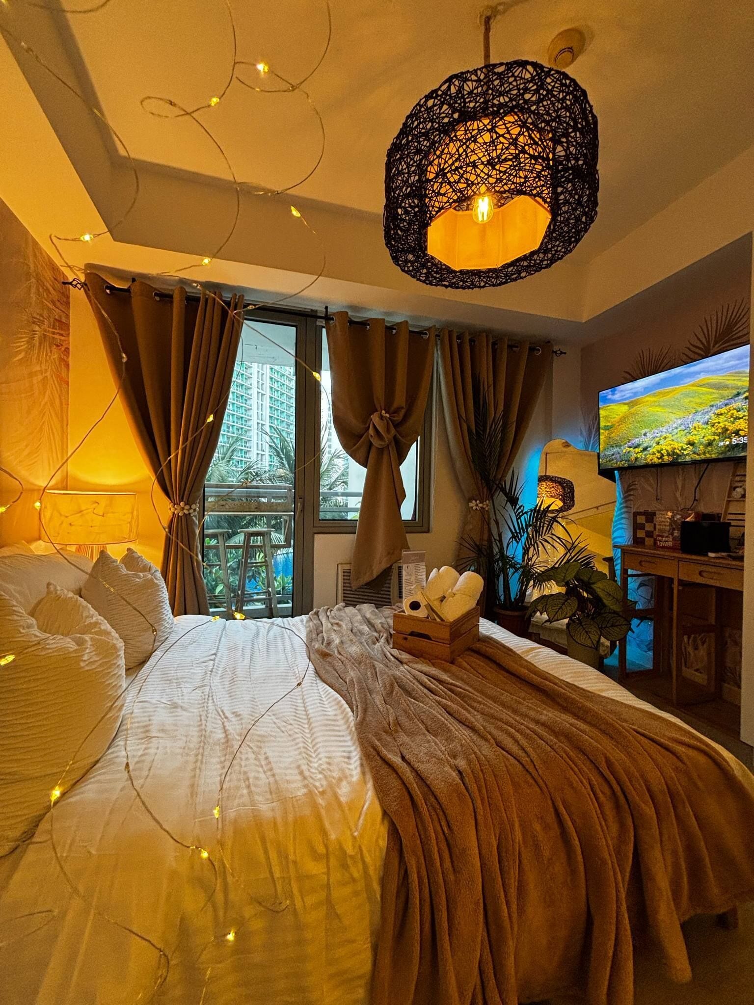 A bedroom with a bed, curtains, a television, and a window with a view of buildings.