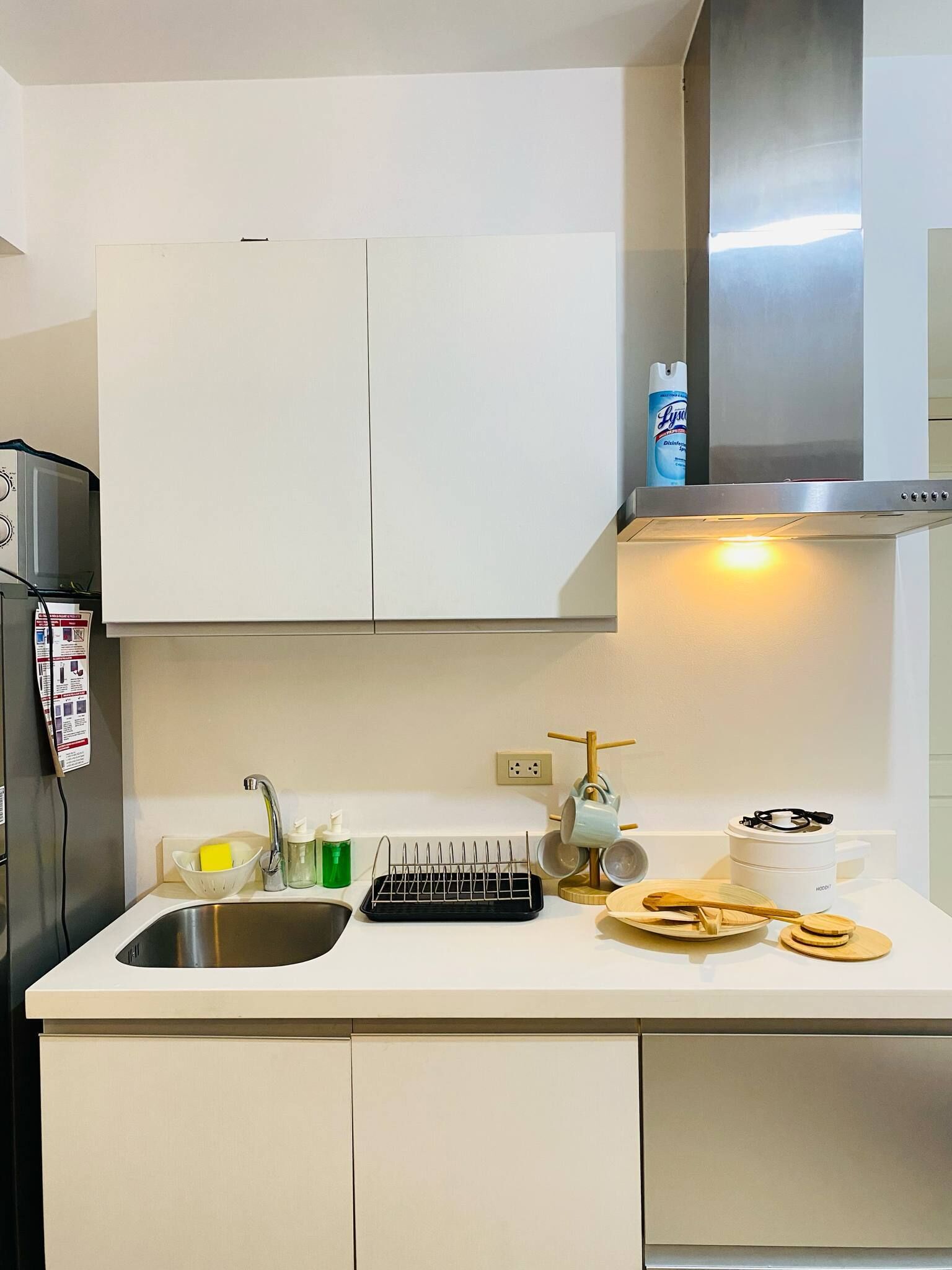 Una cocina moderna con armarios blancos, un lavamanos de acero inoxidable, un escurreplatos, una tetera y un procesador de alimentos.