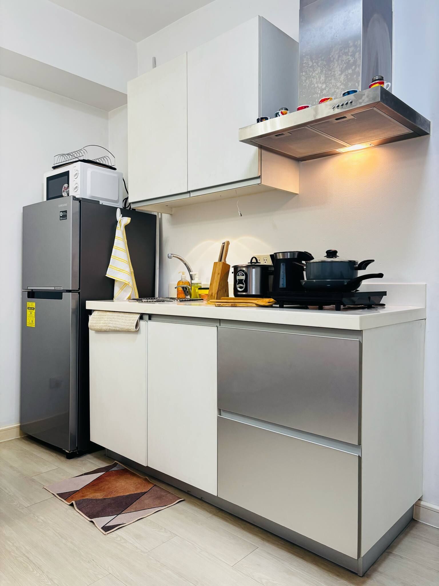 Una cocina compacta con microondas integrado, refrigerador de acero inoxidable, estufa a gas y campana extractora.