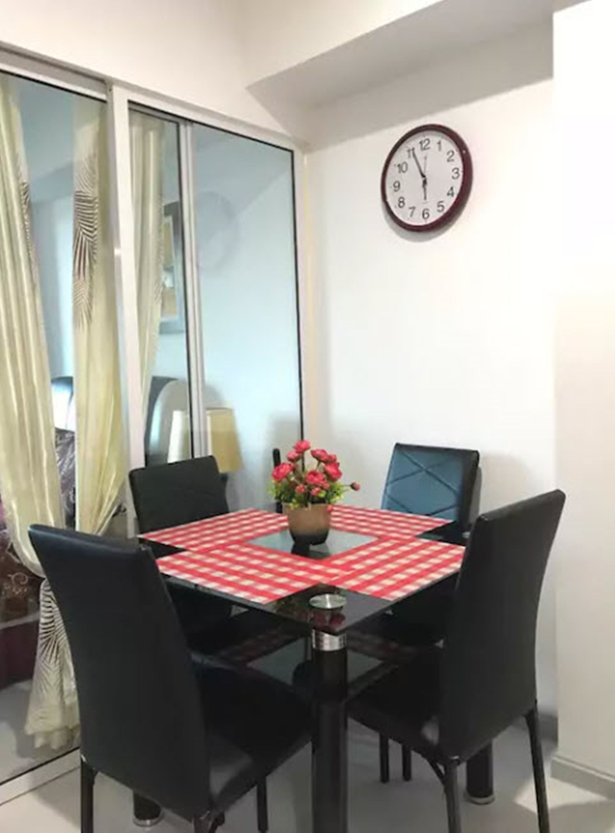 Un comedor con mesa de vidrio, sillas negras y un reloj en la pared.