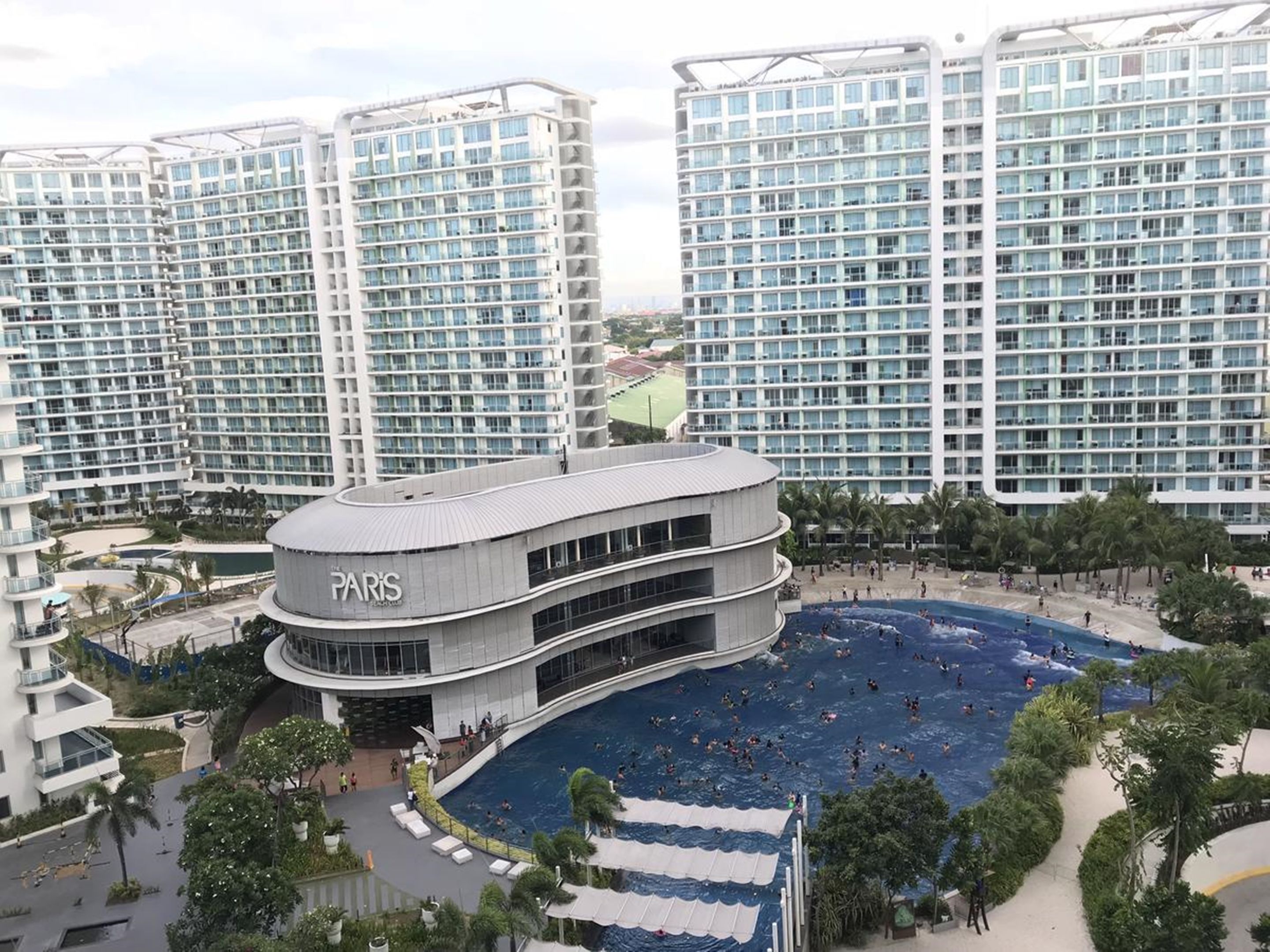 Un hotel moderno con una gran piscina rodeada de palmeras y vistas a rascacielos.