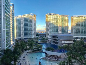 A high-rise hotel with multiple balconies, a central pool area, and palm trees. - Azure Luxury Beach Suites by VacationsPH (Parañaque)