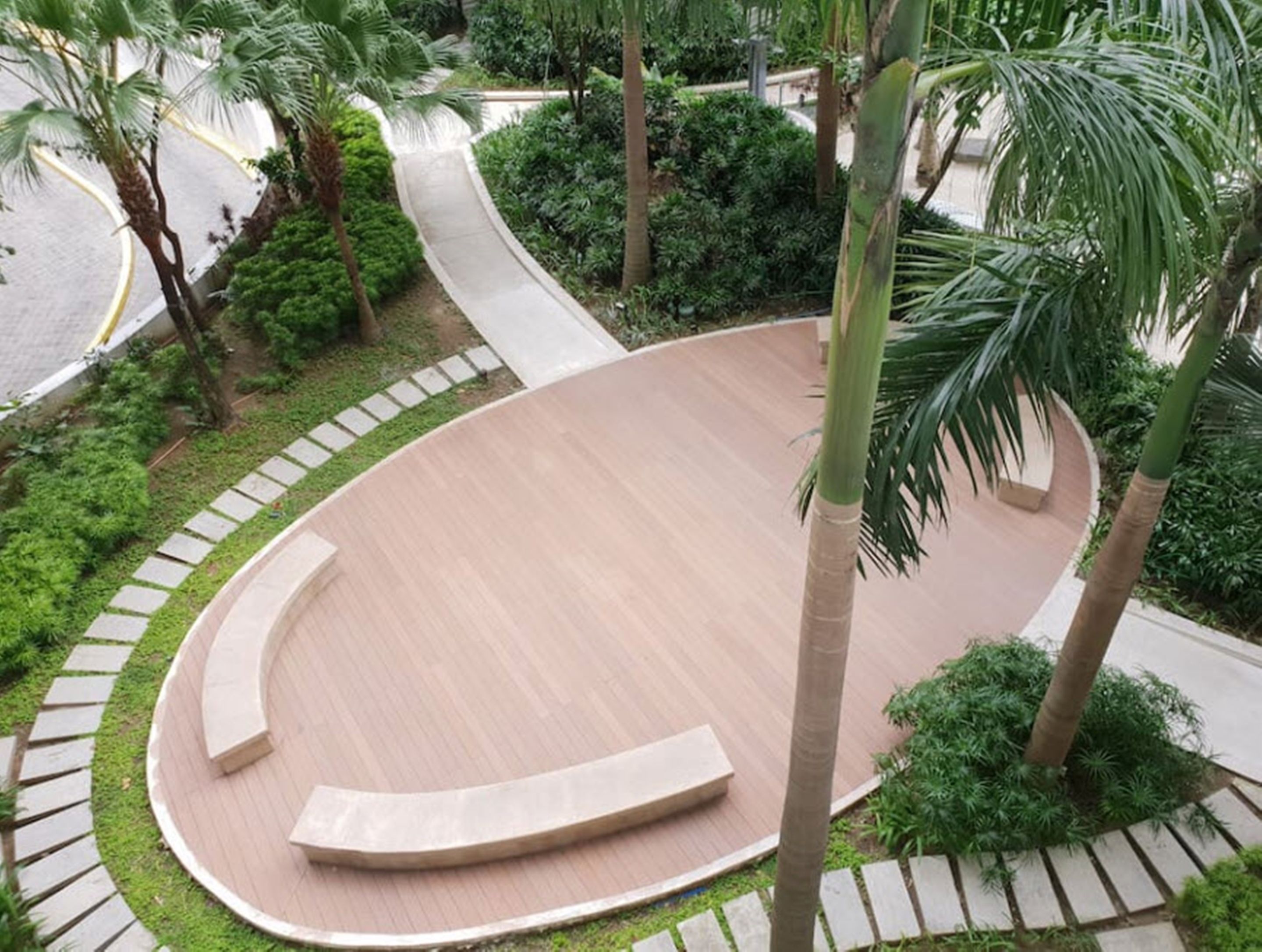 A landscaped area with a curved wooden deck, surrounded by palm trees and greenery.