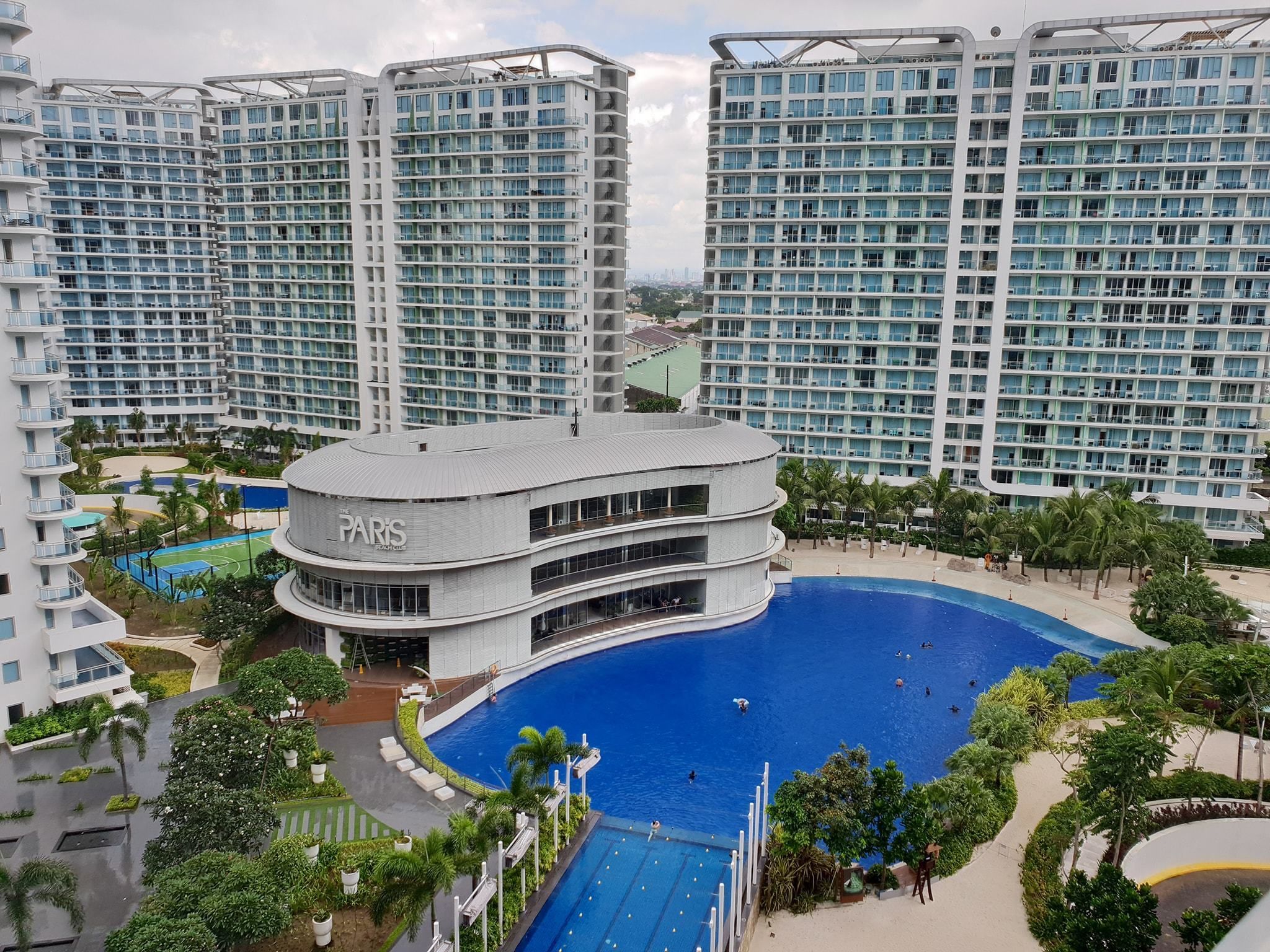 A high-rise hotel with multiple balconies, a central pool, and surrounding greenery.