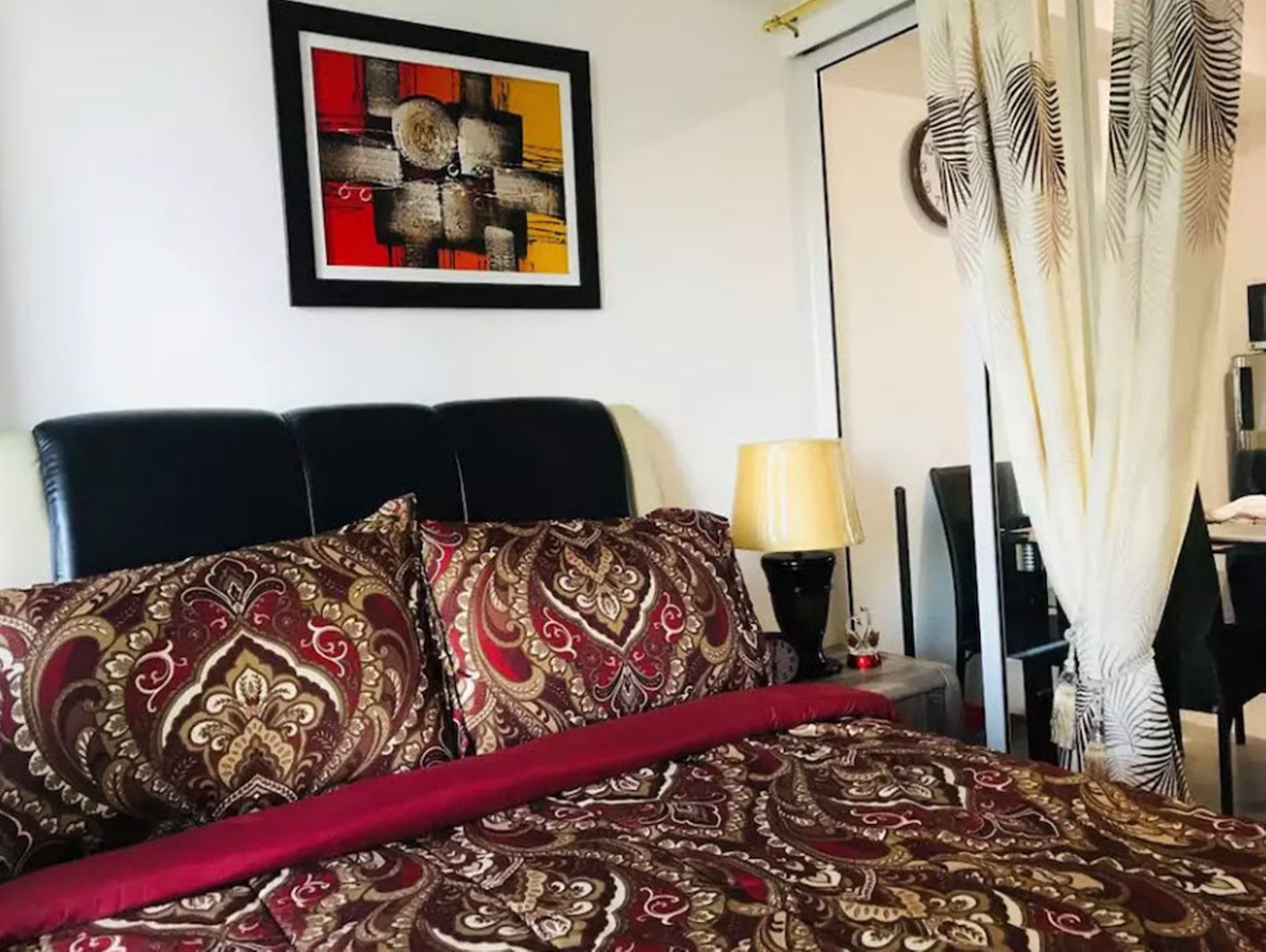 Ein Bett mit gemustertem Überwurf, ein gerahmtes abstraktes Gemälde darüber und eine Lampe daneben.