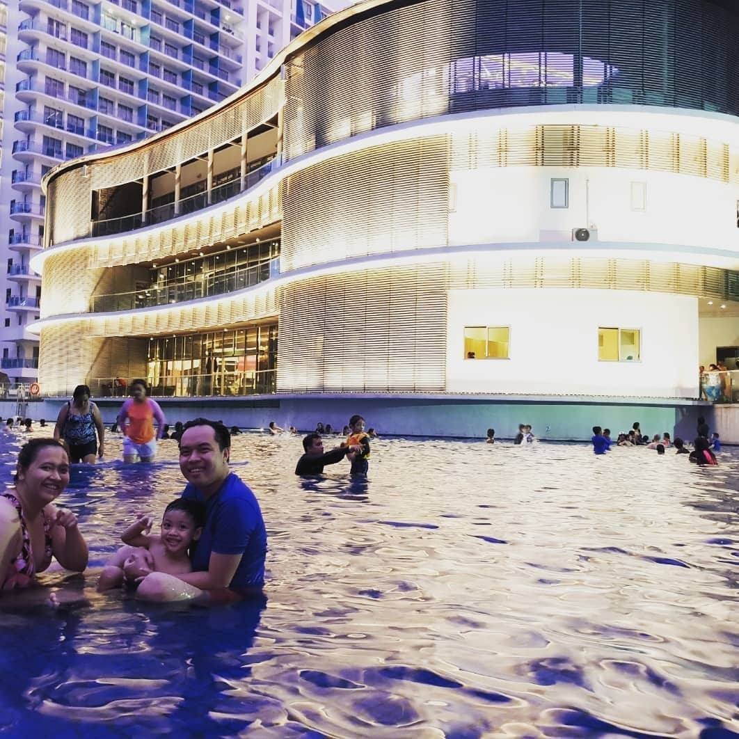 A modern building with a curved facade and a pool area with people swimming and relaxing.