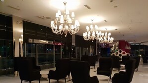 Een moderne lobby met meerdere zwarte fauteuils, een grote kroonluchter en een glazen wand met uitzicht op de skyline.