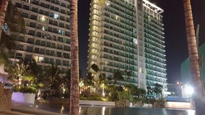 Een hoog hotel met meerdere verdiepingen, een zwembad en palmbomen.