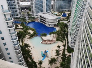 A high-rise hotel with a central swimming pool, a children's play area, and a beach with lounge chairs.