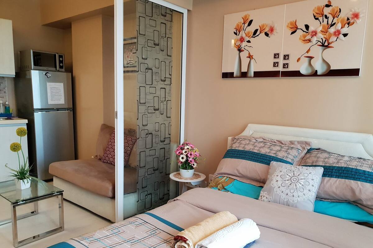 Una habitación de hotel moderna con una cama, una mesita, un refrigerador y un cuadro decorativo.